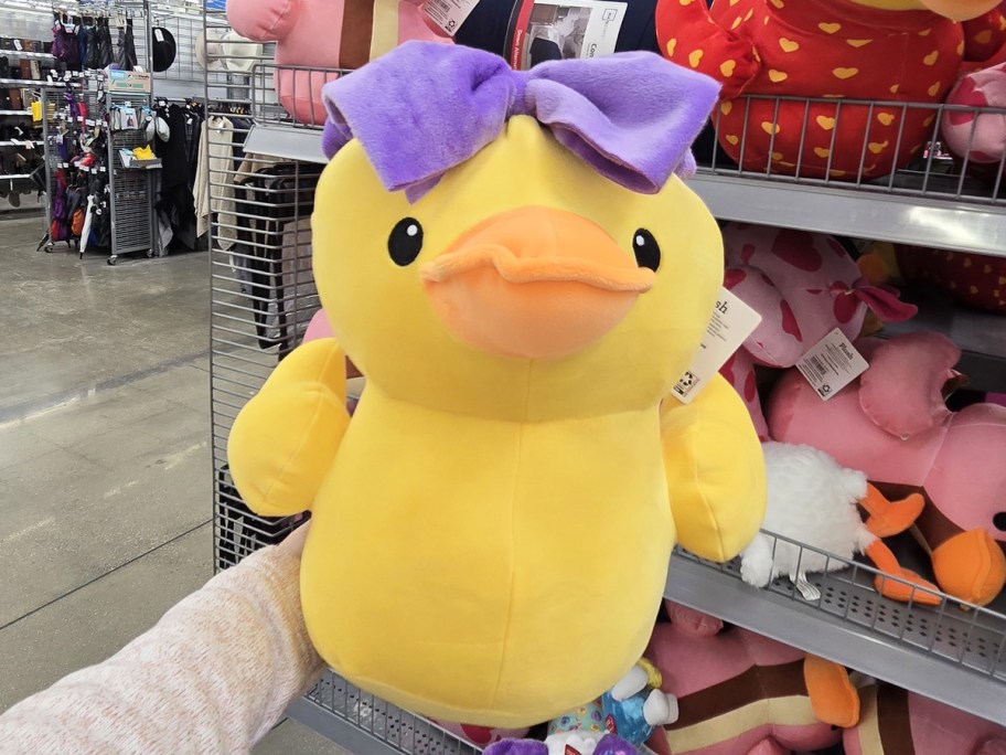 hand holding up a duck plush with a purple bow on top
