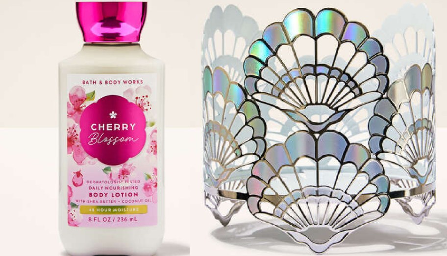 A bottle of Cherry Blossom body lotion with floral design and a pink cap sits beside an iridescent, fan-patterned candle holder on a light background.