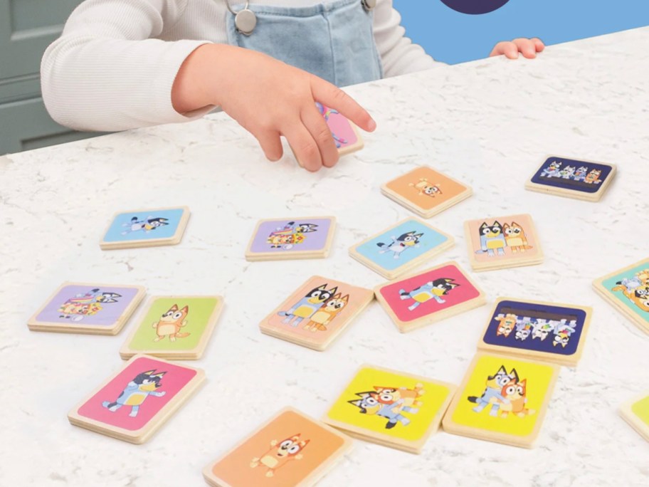 child playing with bluey memory game pieces on table