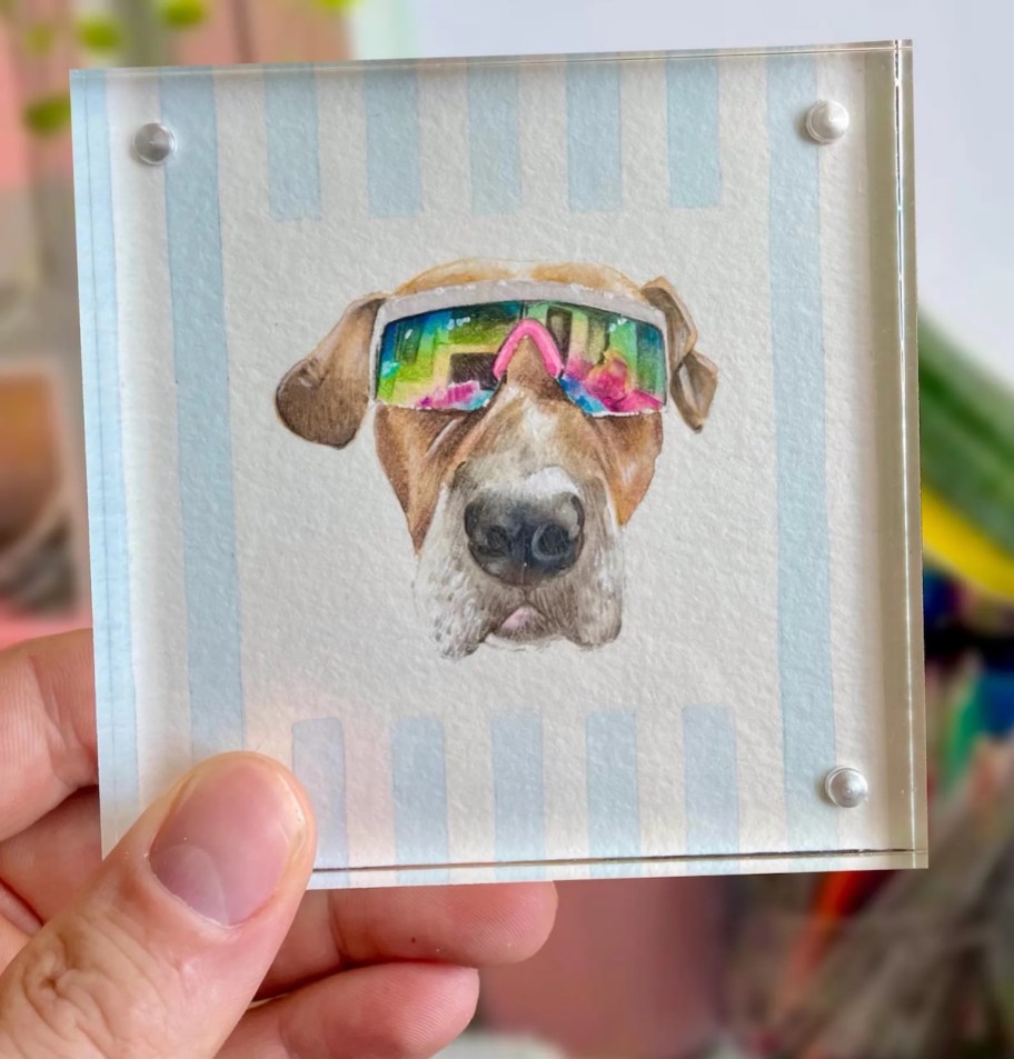 hand holding portrait painting of dog with sunglasses