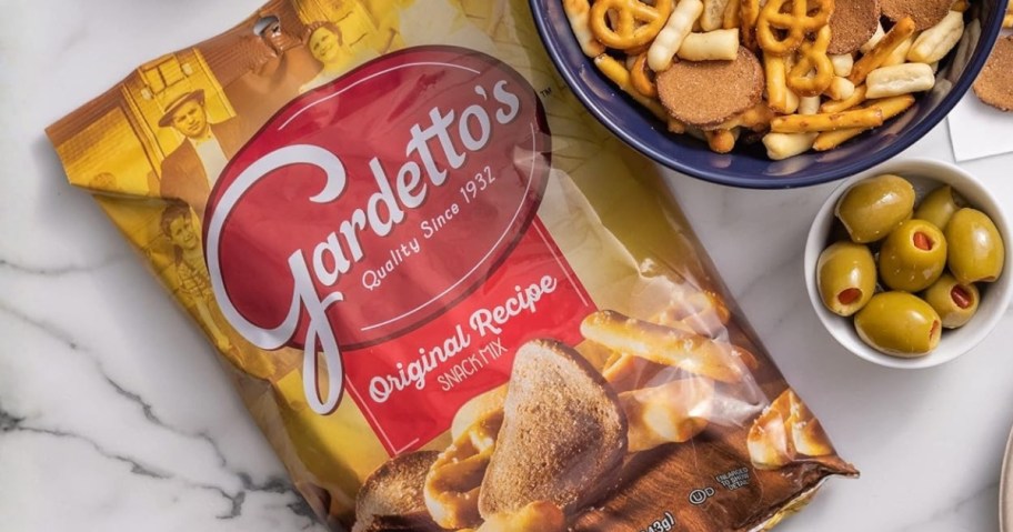 a bag of Gardettos chips next to a bowl with some in it and a bowl of olives