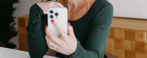 Woman holding white apple iPhone while sitting at table and wearing green shirt