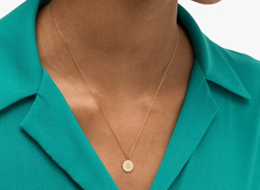 close up of woman wearing gold initial necklace and teal blue shirt