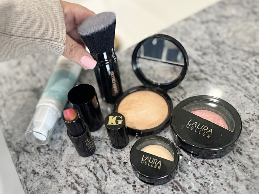 hand reaching for laura geller brush with makeup on counter
