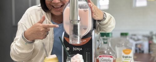 a woman points to a ninja slushi machine as she dispenses a frozen drink into a glass from the machine
