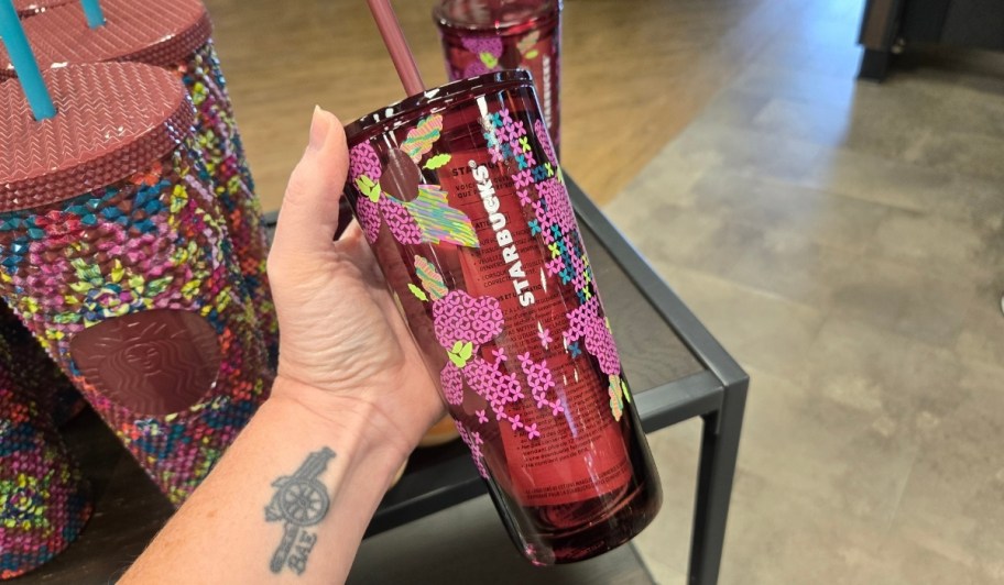 womans hand holding a cold cup with cross stitch design