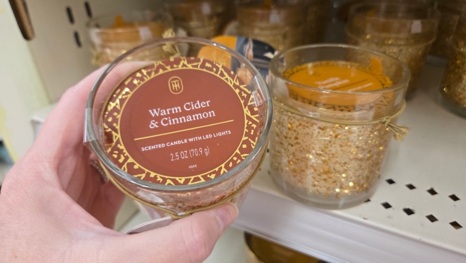 hand holding warm cider and cinnamon candle on store shelf
