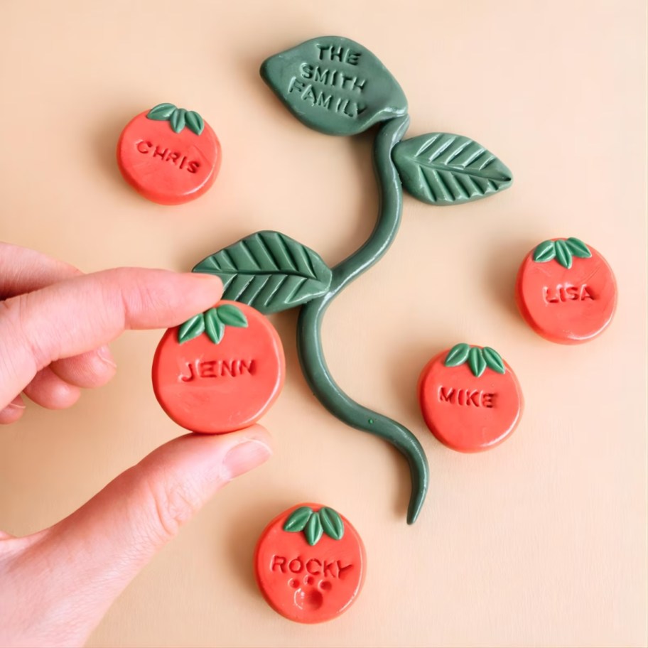 Hand holding a tomato clay magnet with name