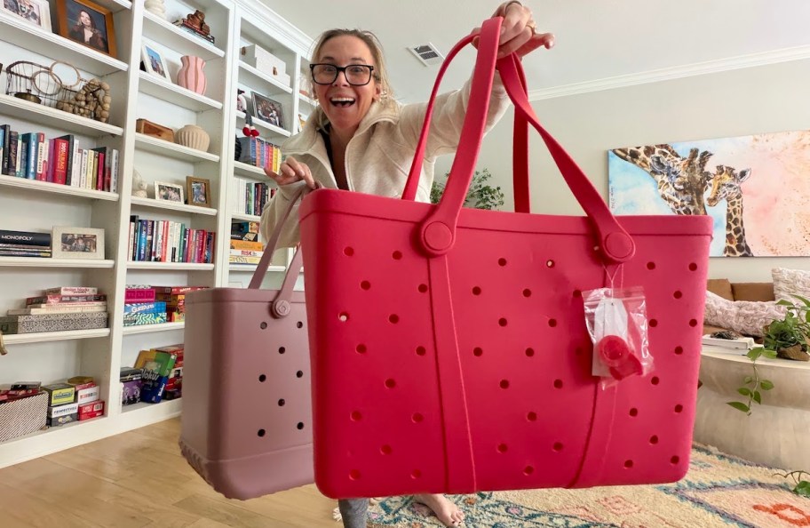 woman holding bright and dusty pink bogg bags in living room with bookshelves