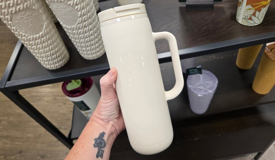 womans hand holding white travel mug