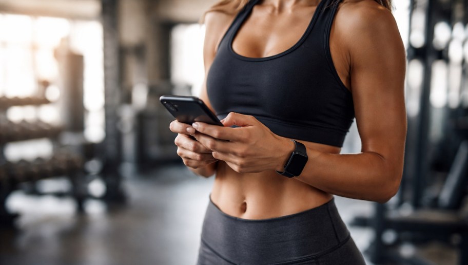 person standing in gym with athletic clothes holding phone