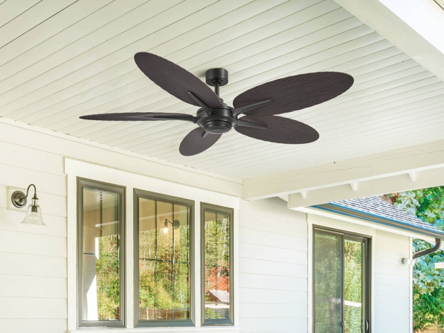 a large black palm leaf style outdoor ceiling fan on a porch