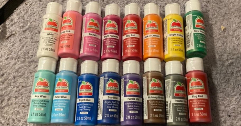 several bottles of different color apple barrel paints laid out on a carpet