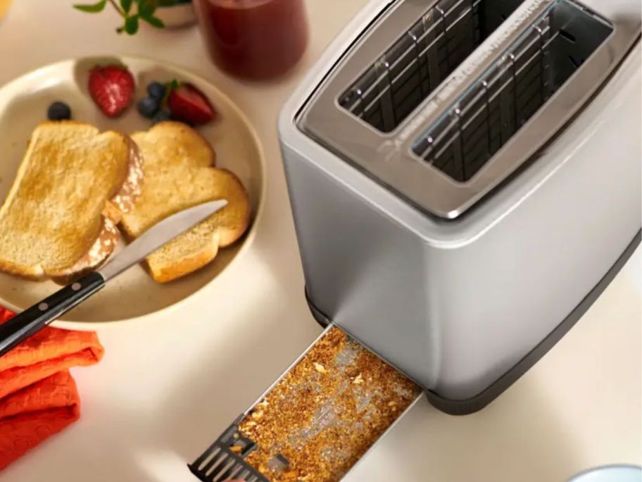 Bella PRO 2-Slice Toaster in Stainless Steel with crumb tray opened and surrounded by food 