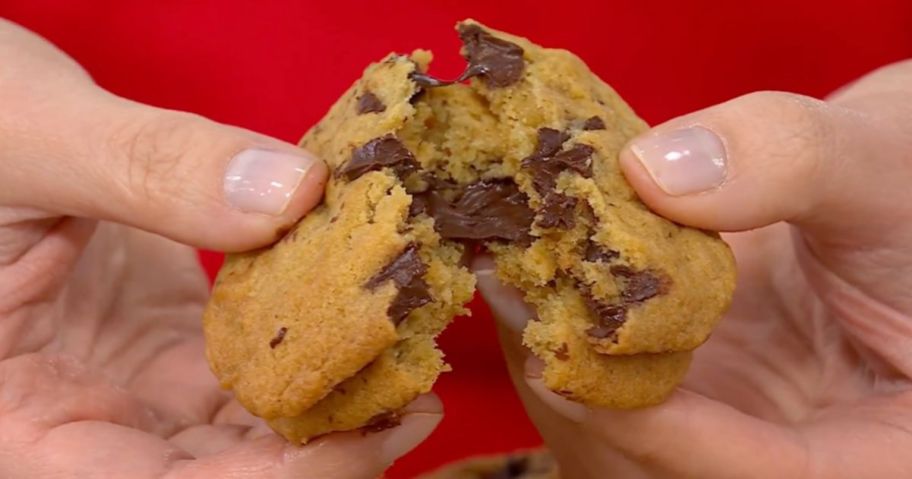 Hand breaking apart two stacked chocolate chunk cookies