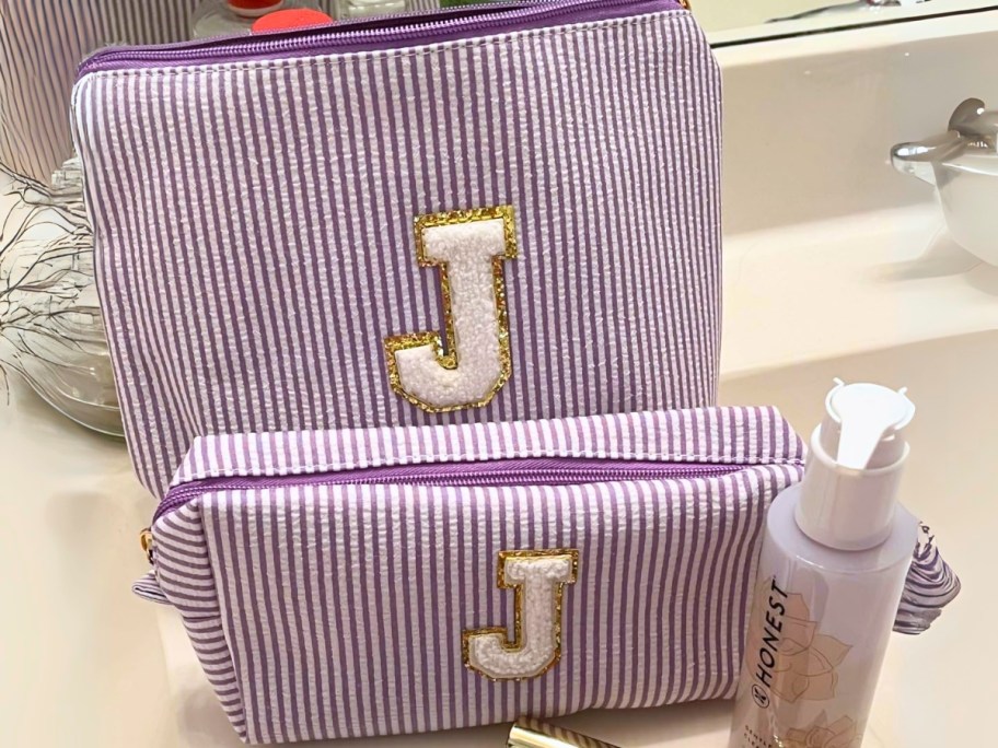two cosmetic zipper bags with purple stripes and the initial "J" on them with makeup