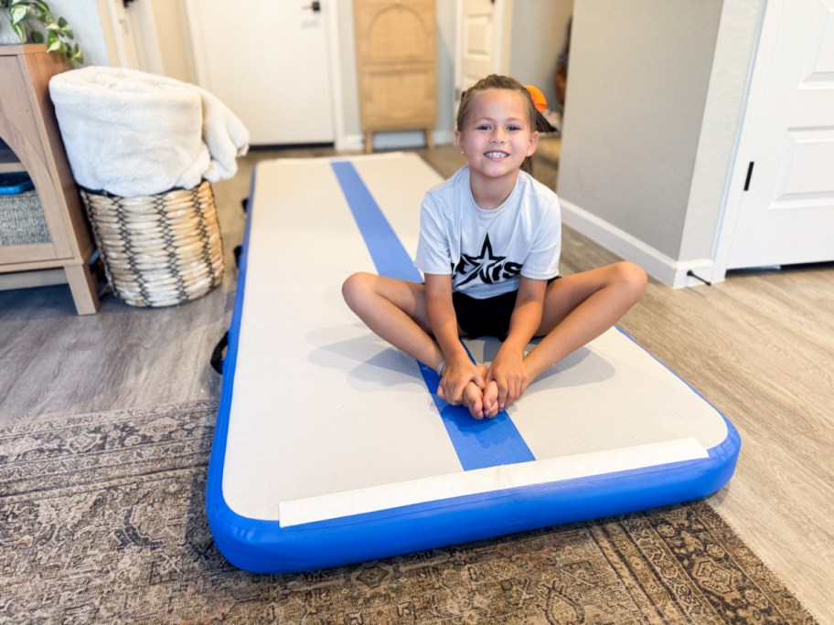 Young girl, sitting on blue and white striped gymnastics mat inside home
