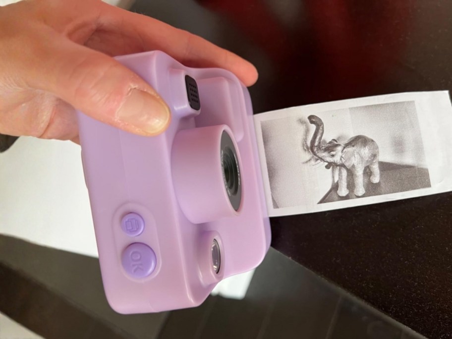 hand holding a purple kids instant print camera, picture printing out of it