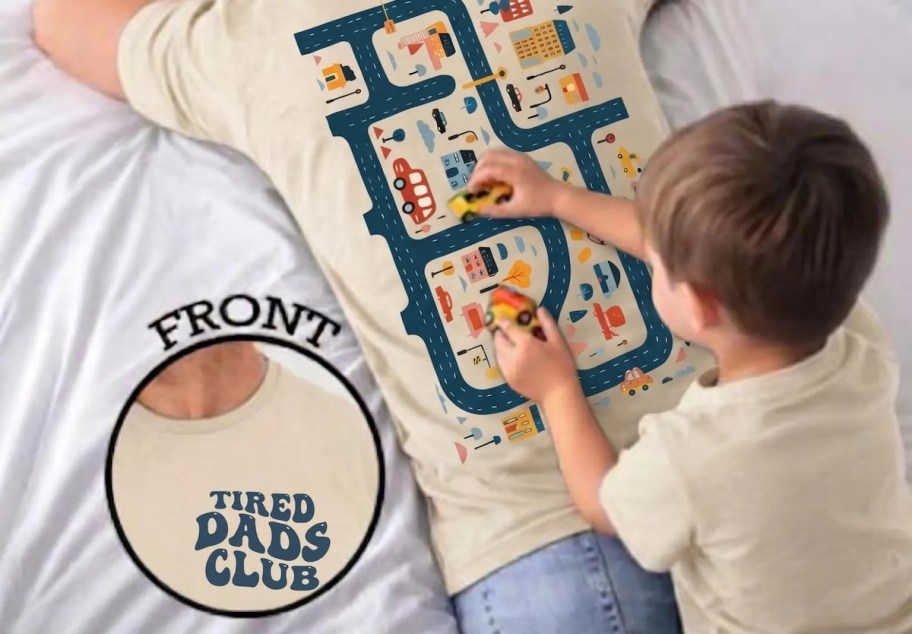 Boy playing cars on roadmap T-shirt with dad laying on floor 