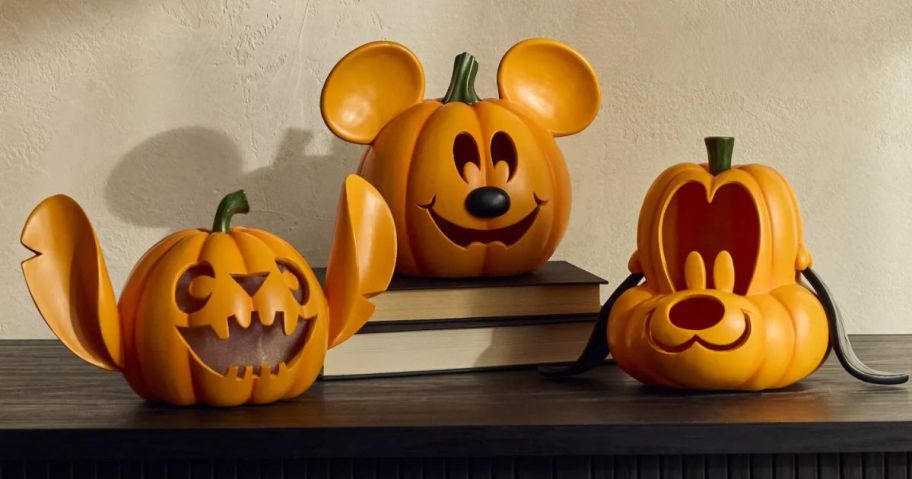 A Stitch, Mickey Mouse, and Goofy LED Pumpkin on a piece of furniture and a stack of books