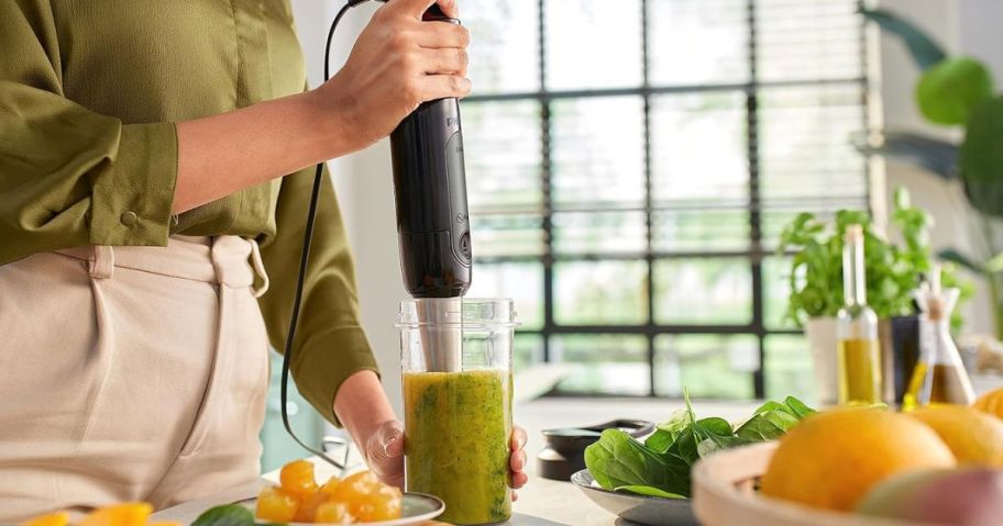 Hand using a Philips hand blender to make a green sauce