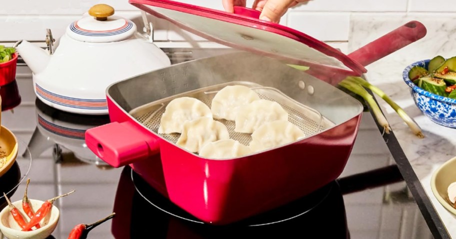 person taking glass lid off a red square pan with dumplings inside