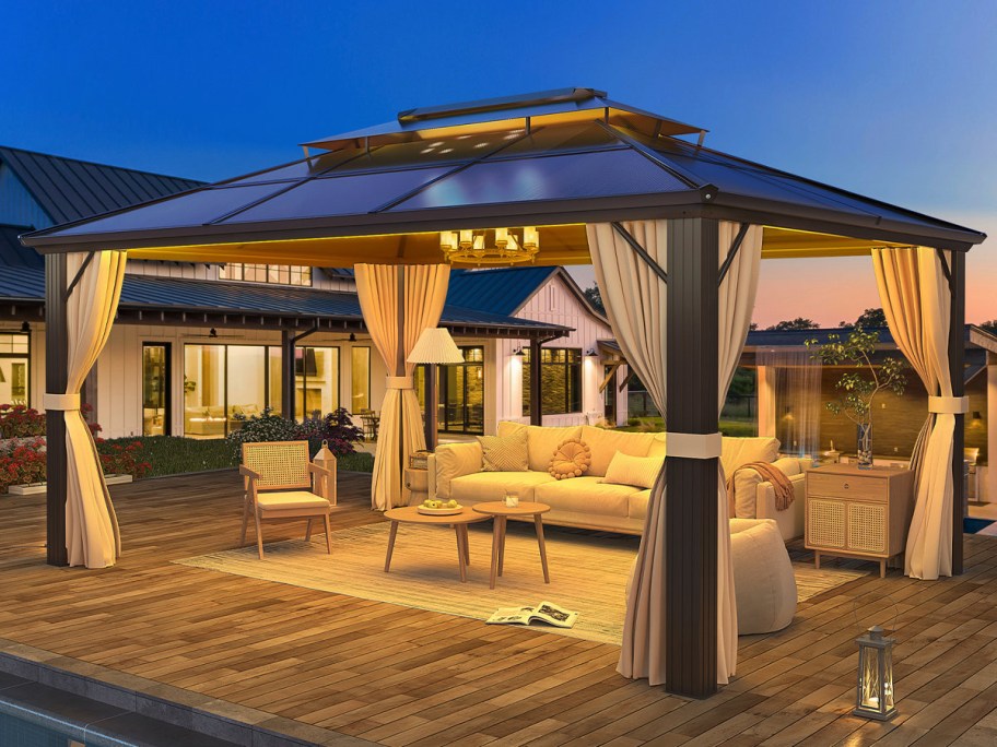 A cozy patio setup at dusk features a large gazebo with draped curtains.