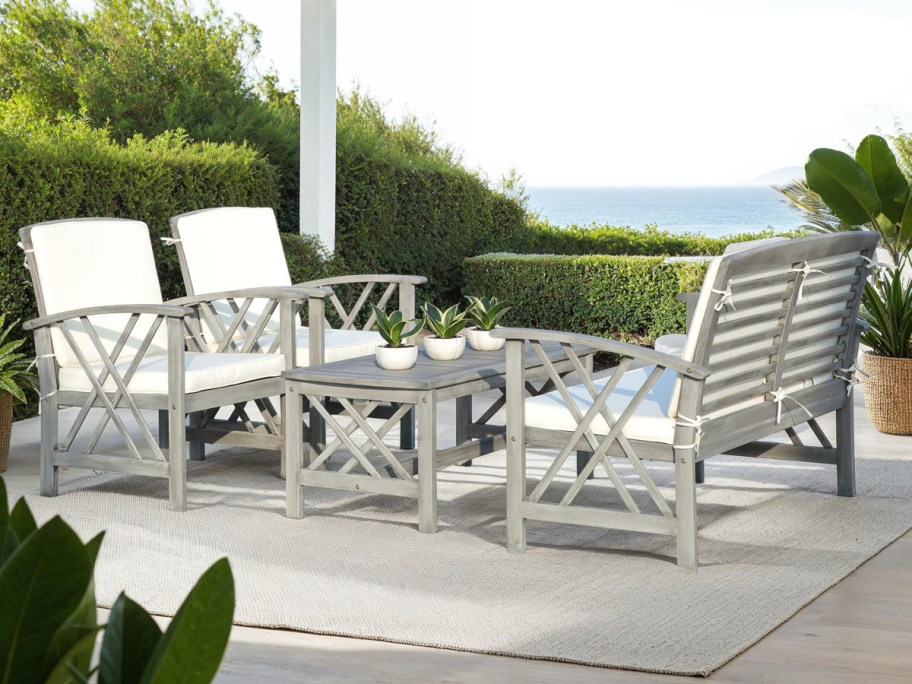 Outdoor patio with white cushioned wooden furniture set, table adorned with small potted plants.