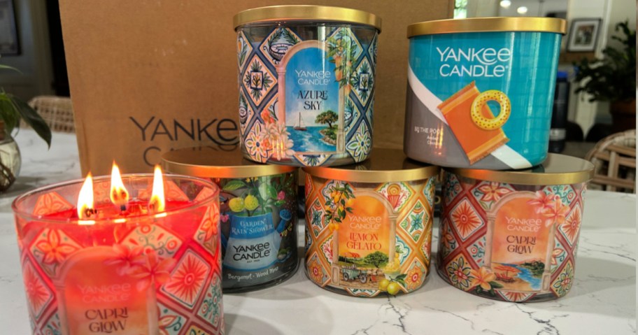 different Yankee candle stacked up on white kitchen counter with one lit candle.