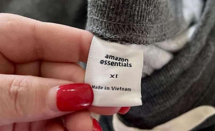 a woman holding an amazon essentials clothing tag