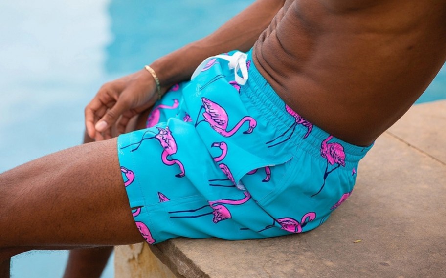 a man sitting by the edge of pool in a pair of flamingo swim trunks