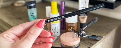 hand holding up a black eyeliner with lots of elf makeup products in the background