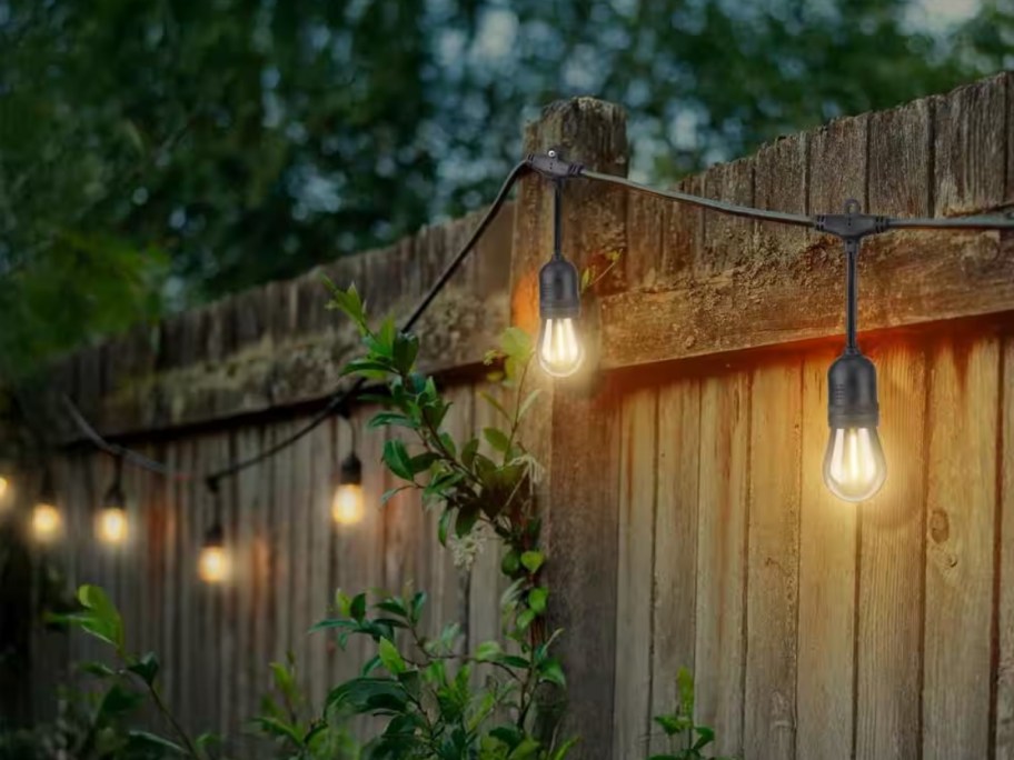 a set of string lights draped on a wooden privacy fence 