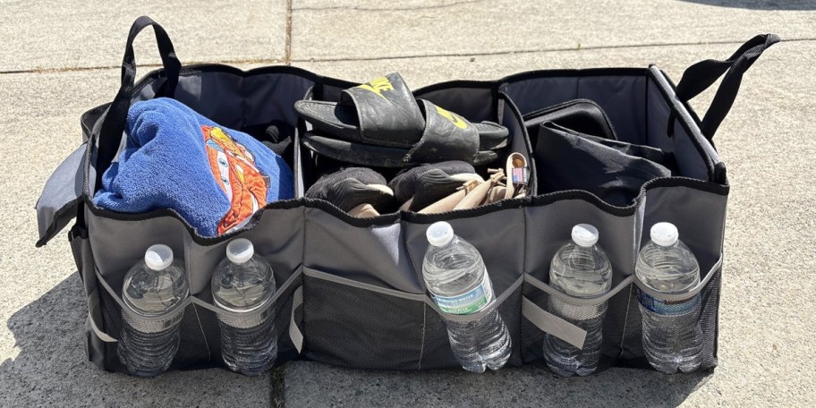 gray and black trunk organizer with shoes, water bottles, and clothes inside
