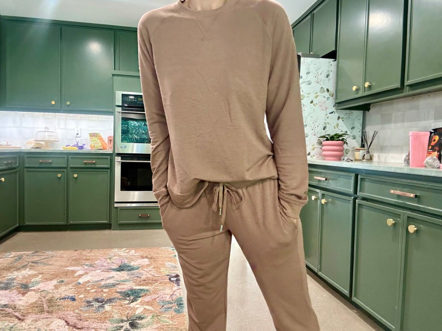 woman wearing tan long sleeve top and joggers in kitchen