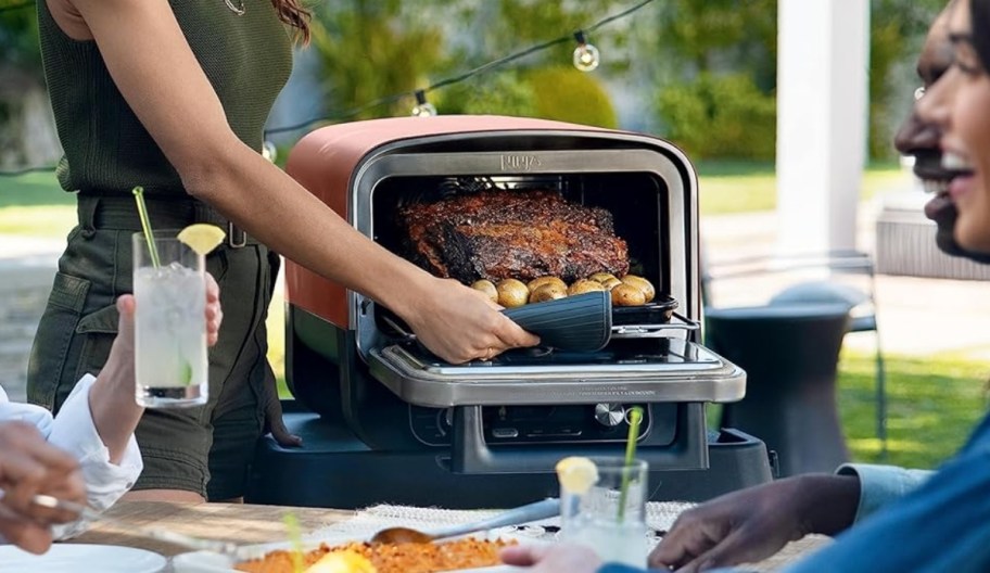a womans hand removing a roast from a ninja outdoor grill
