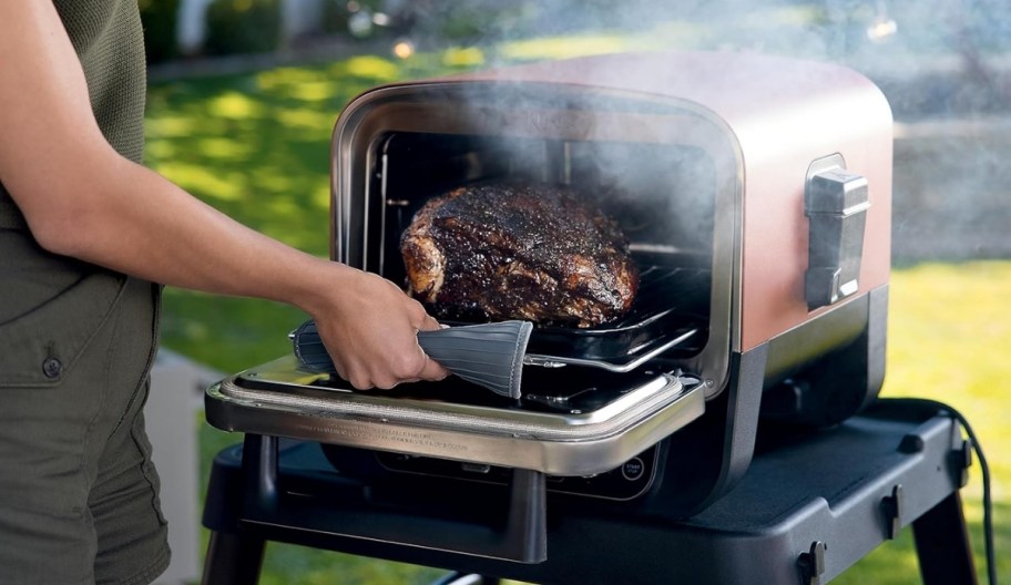 a womans hand removing a brisket from a ninja outdoor grill