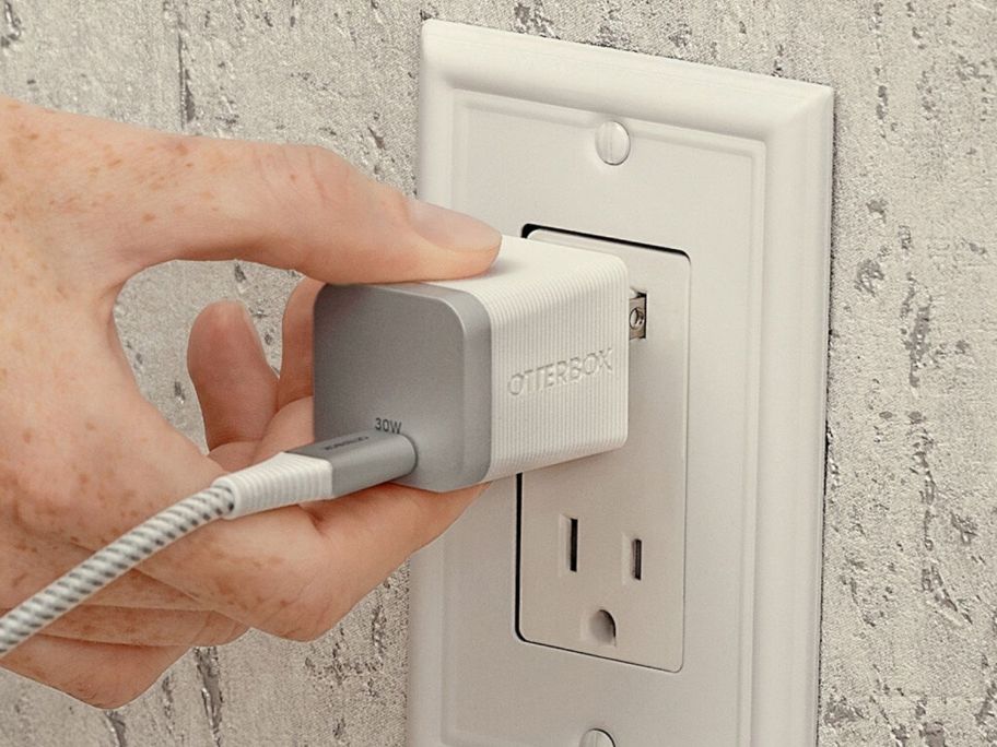 person plugging in otterbox charger into wall outlet