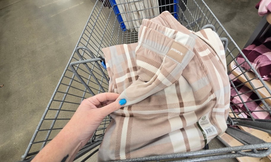 a womans hand holding the waistband of a plaid of taupe colored plaid pajama pants