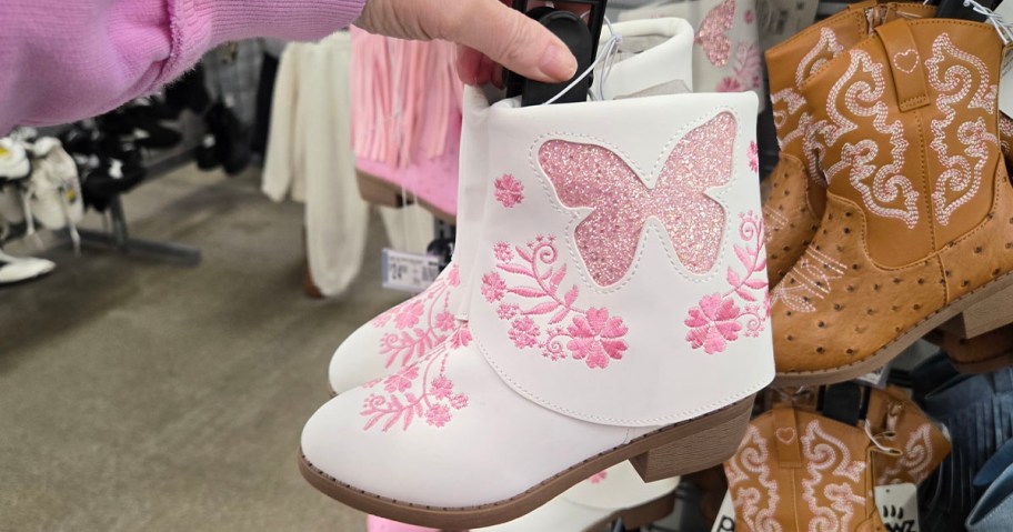hand holding pair of white boots with pink butterflies 