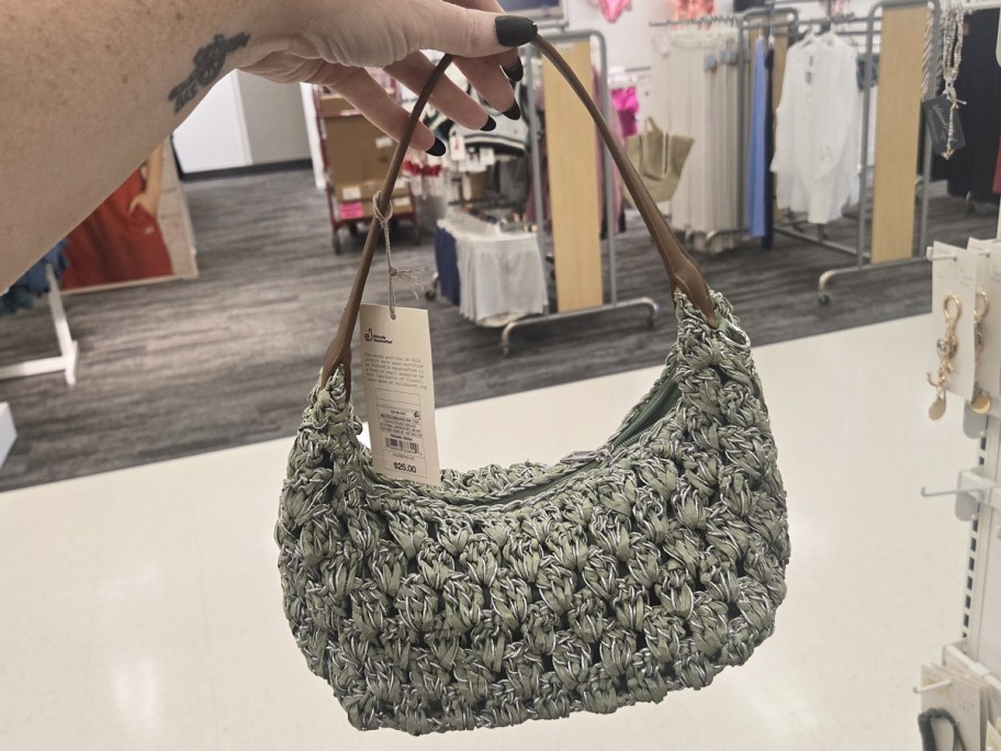 hand holding up a green straw shoulder bag in store