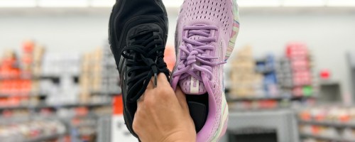 Woman holding a pair of black and purple Brooks running shoes inside store