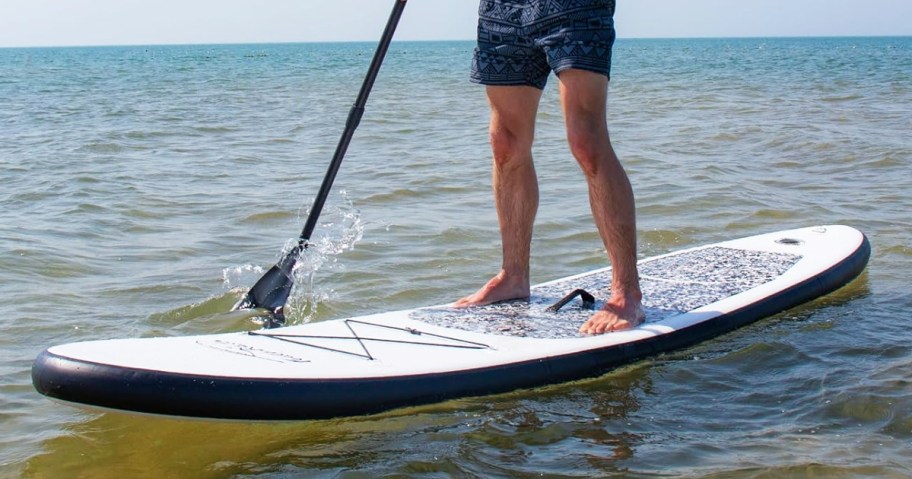 man standing on a white and black paddle board in water