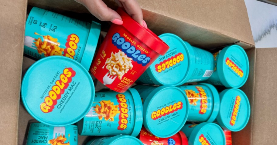 hand reaching for an individual cup of Goodles Mac & Cheese in a box with more of them