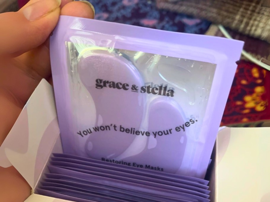 hand pulling a set of Grace & Stella purple under-eye masks out of a box