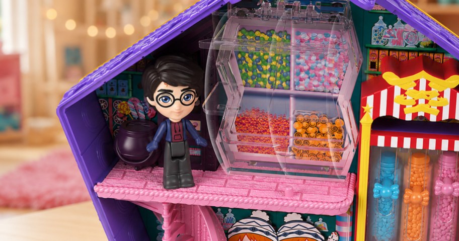 Harry Potter figure standing inside the Chocolate Frog compact beside a colorful Honeydukes candy display in a playroom setting.