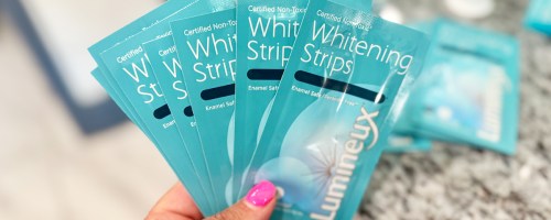 hand holding blue packets of Lumineux Teeth Whitening Strips