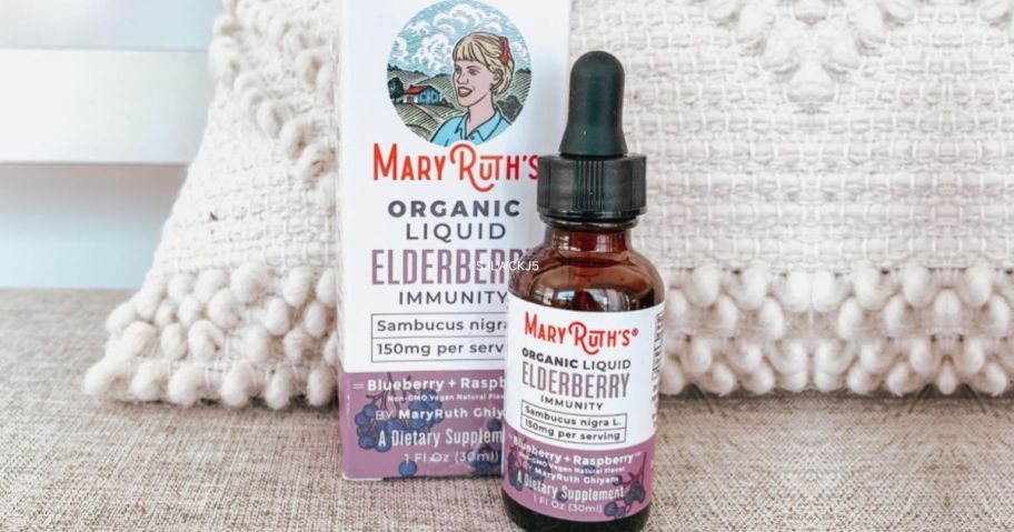 A bottle of Mary Ruth's Organic Liquid Elserberry Drops in front of a throw pillow