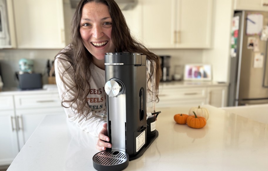 woman holding a black ninja single serve coffee maker on kitchen counter