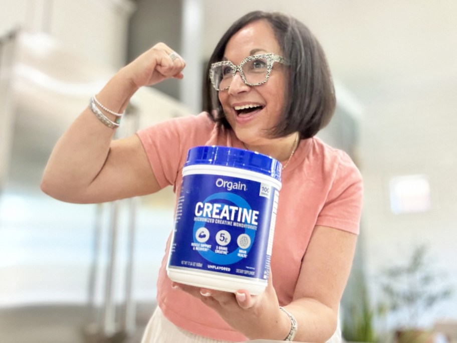 woman in a pink shirt holding up a blue canister of Orgain Creatine